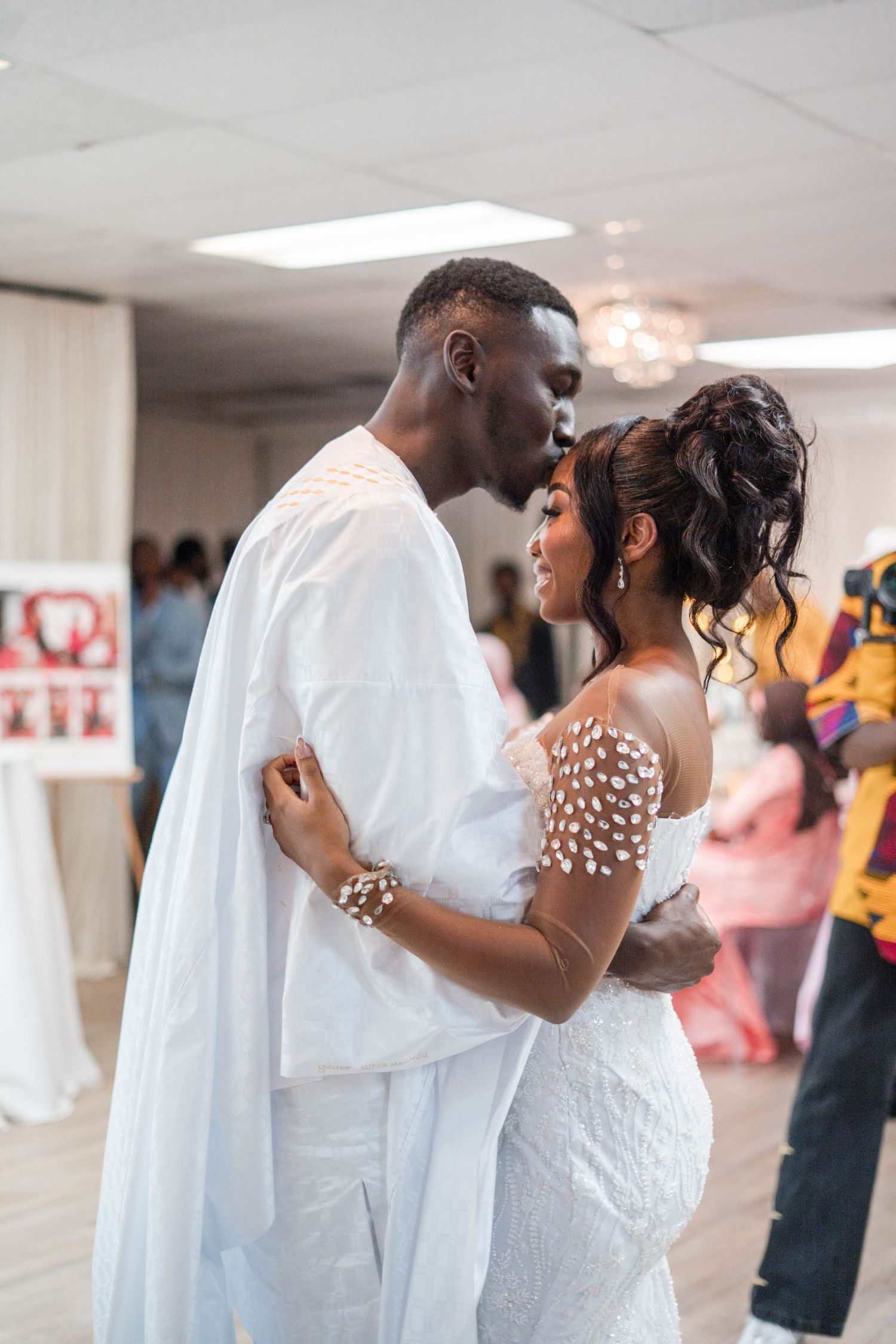 Bride and groom share romantic first dance kiss at wedding reception, groom in traditional white attire.