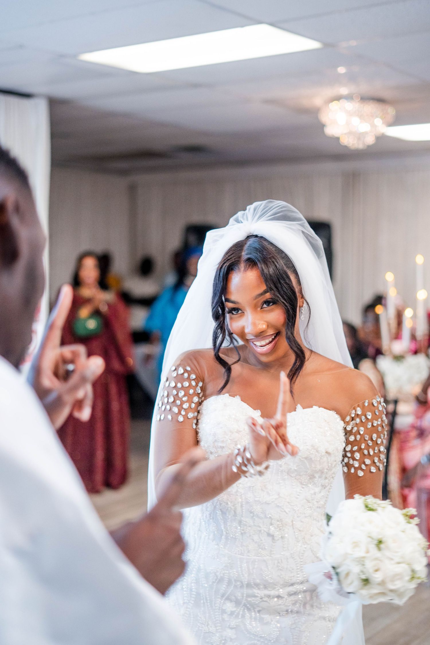 Radiant Black bride in embellished off-shoulder wedding gown and veil smiles during wedding ceremony.