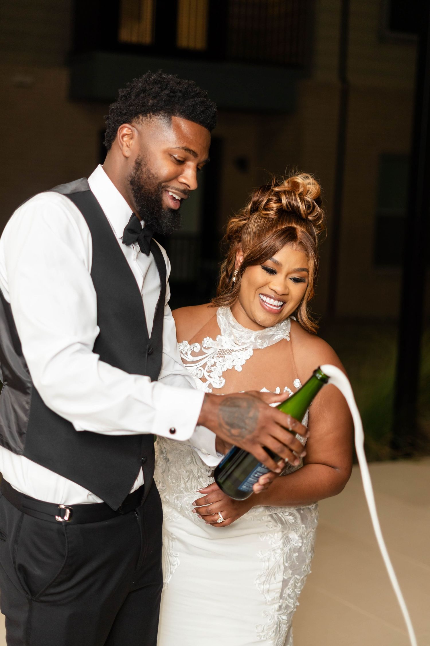 Joyful newlywed couple popping champagne bottle together at their wedding reception celebration.