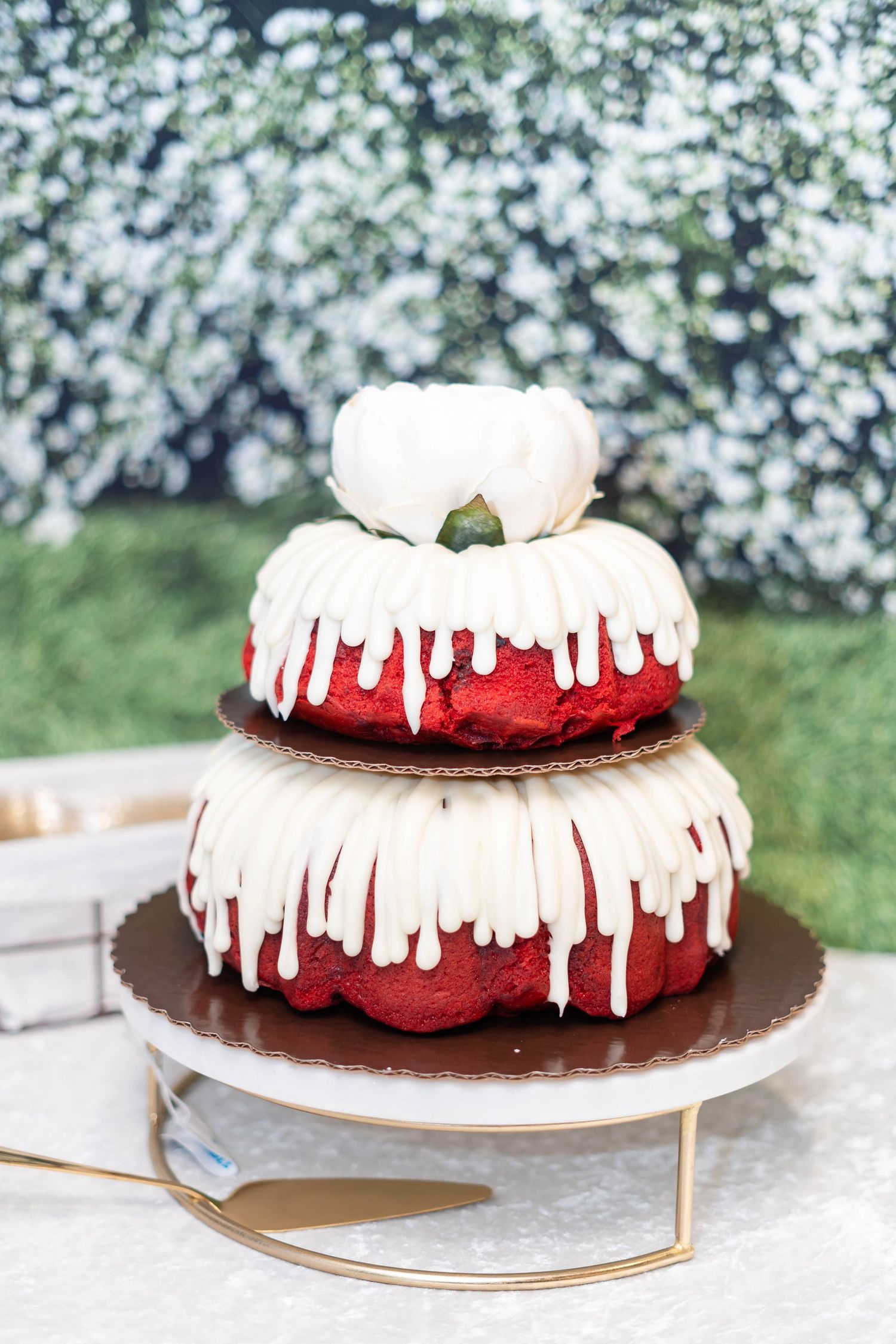 Three-tiered red velvet bundt wedding cake with white cream cheese frosting drizzle on a white cake stand.