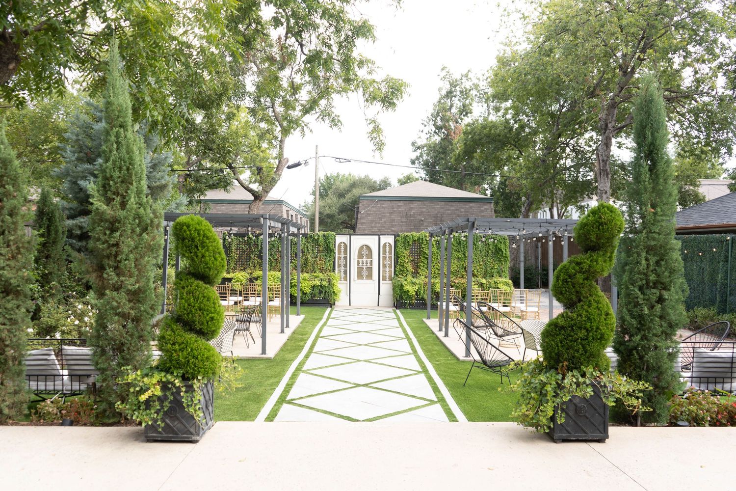 Elegant outdoor wedding venue garden pathway with manicured topiaries leading to white chapel entrance.