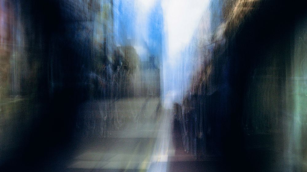 A blurred motion photograph of a street scene with buildings and trees creating an abstract urban composition.