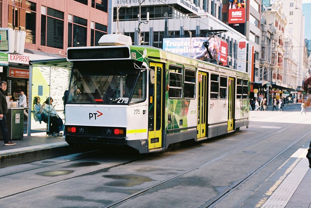 Modern yellow and green trams line up on city streets with buildings and urban infrastructure in the background.
