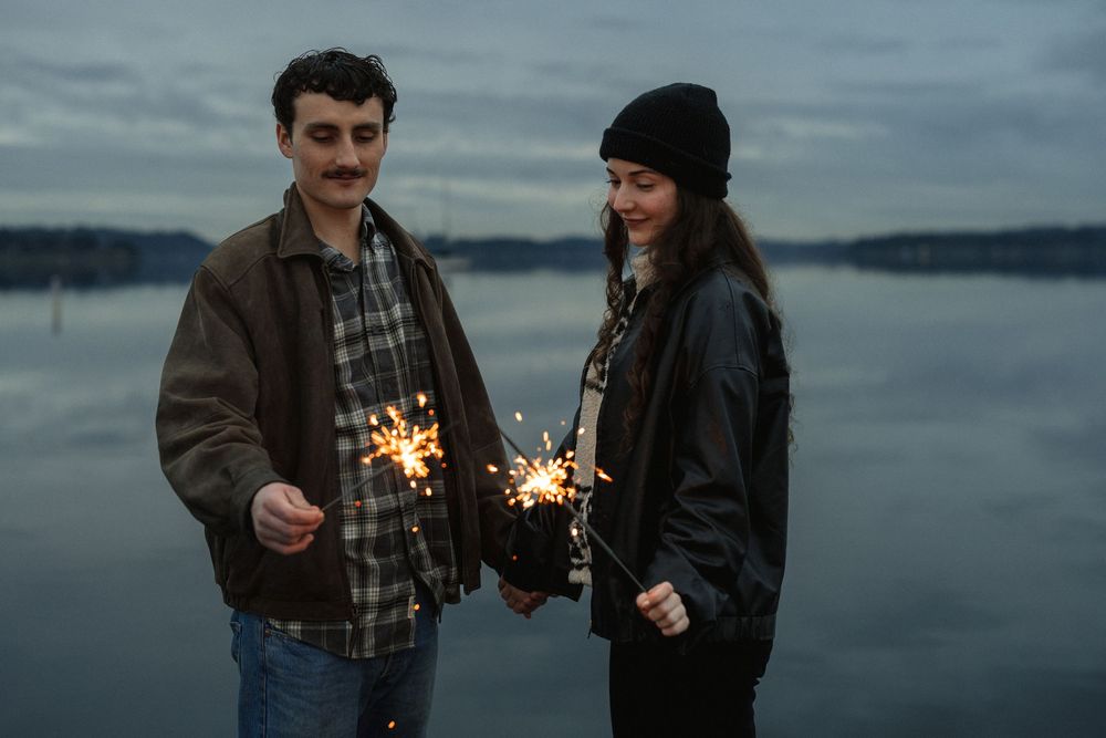 A couple holds sparklers while enjoying a romantic evening by a waterfront at dusk.