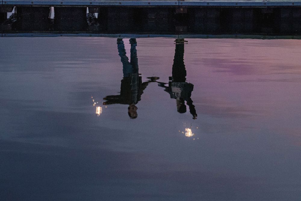 Silhouettes of people walking on a reflective surface at dusk with warm lighting in the background.