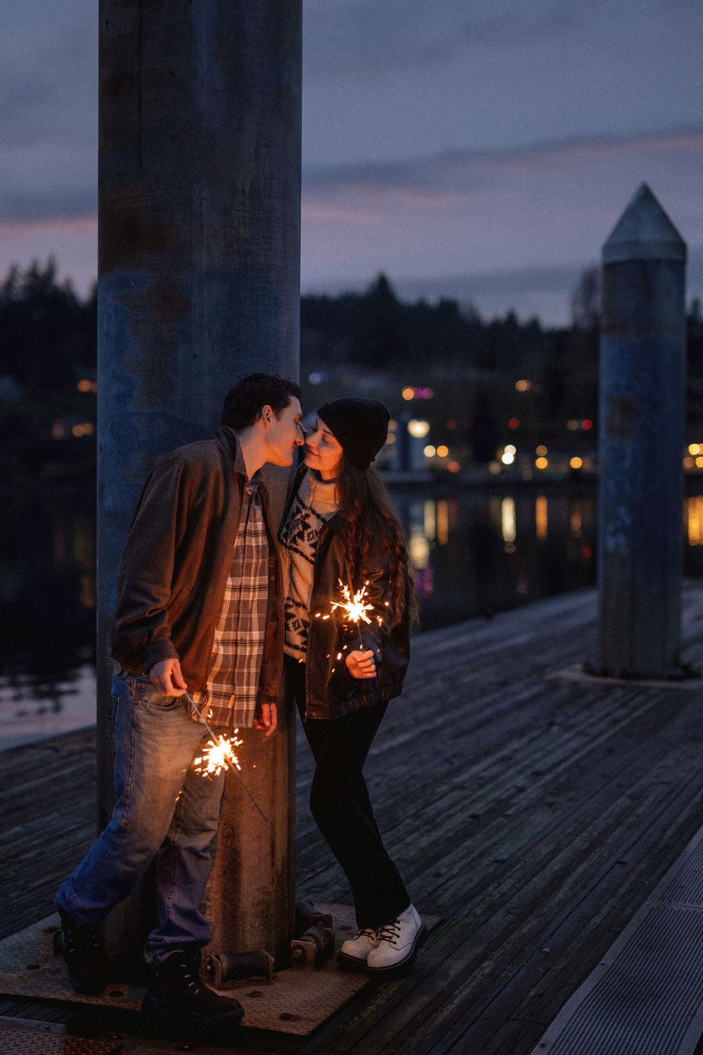 Silhouettes of figures on a wooden dock light sparklers against a dusky purple evening sky.
