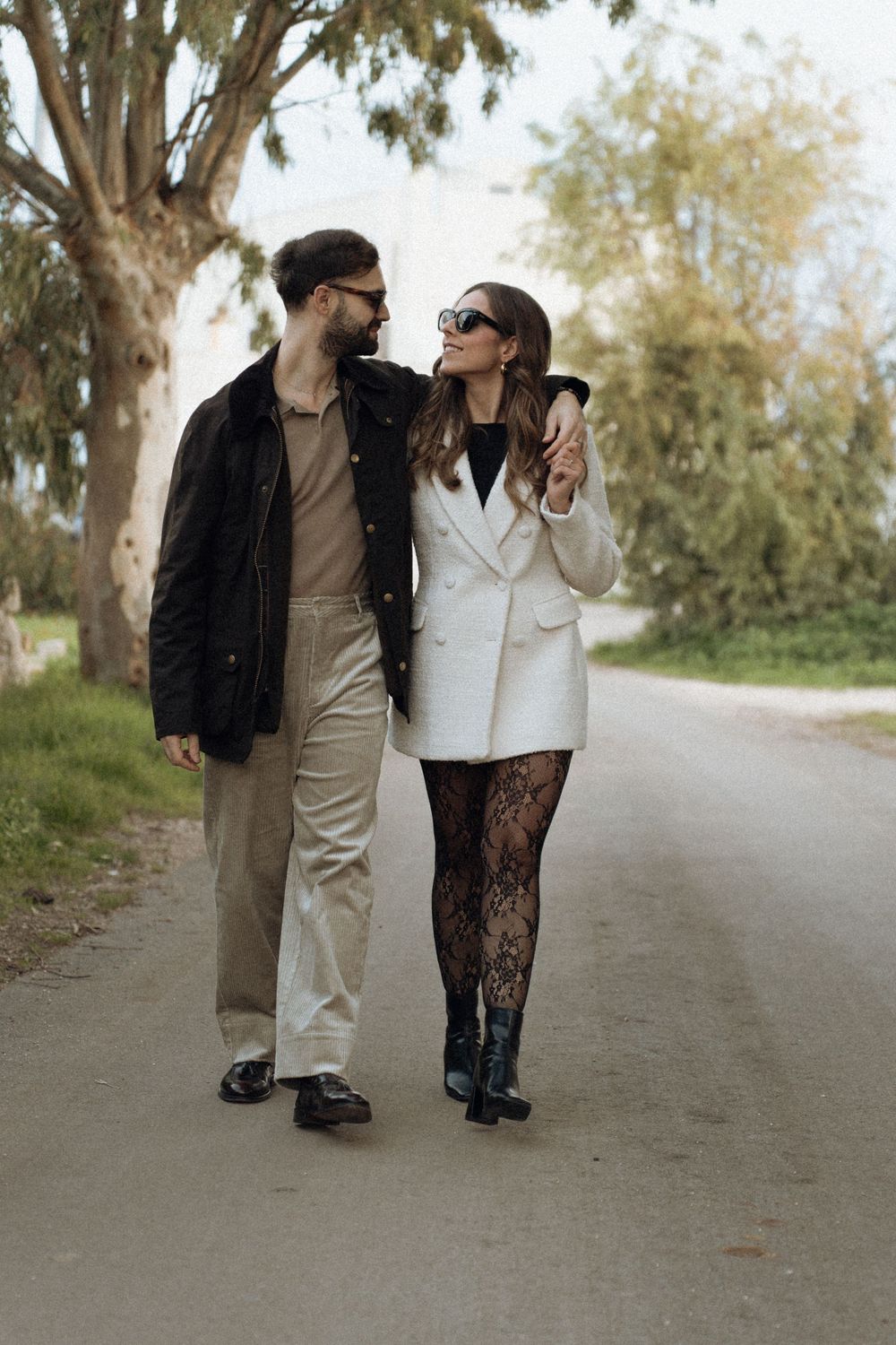 A couple walking together on a tree-lined path in casual attire on an autumn day.