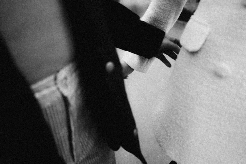 A close-up black and white photo shows hands gently holding a small kitten with closed eyes.