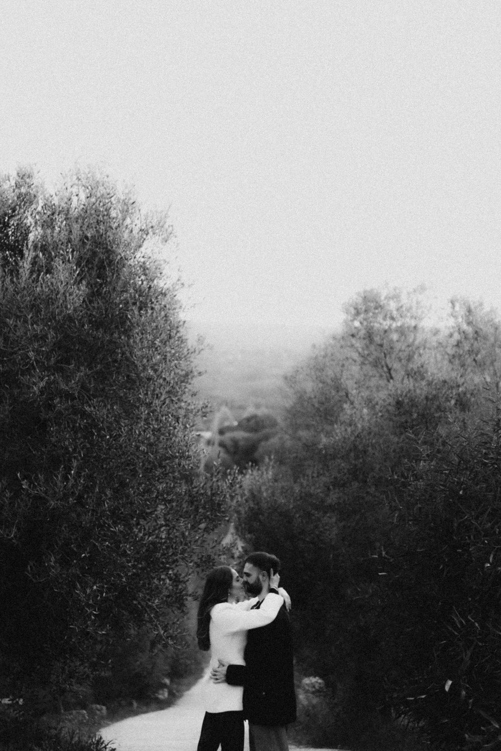 A romantic couple embraces in a black and white photo series against a backdrop of trees and natural scenery.