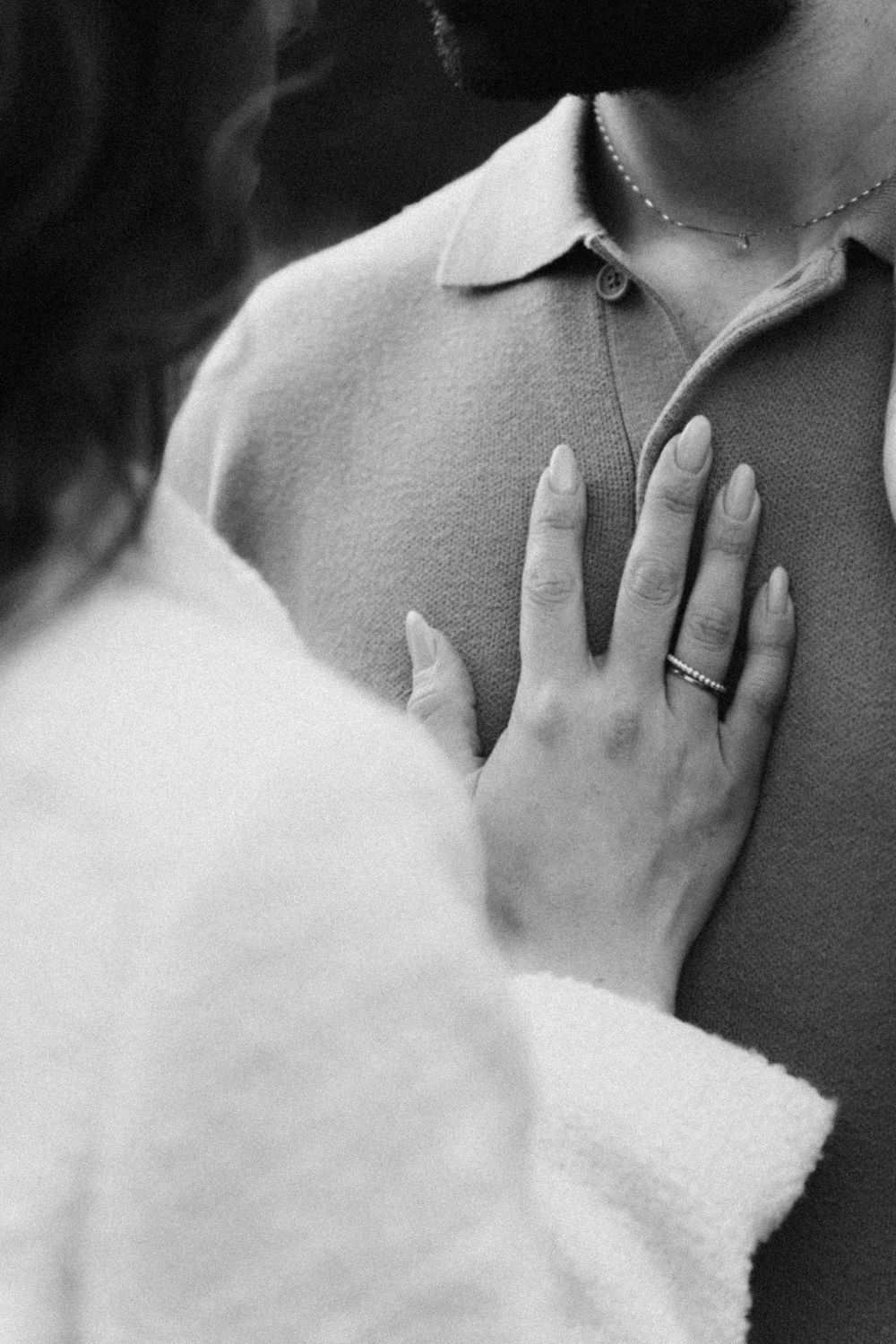 Black and white close-up photograph of a person wearing a white collared shirt with hand near their neck.