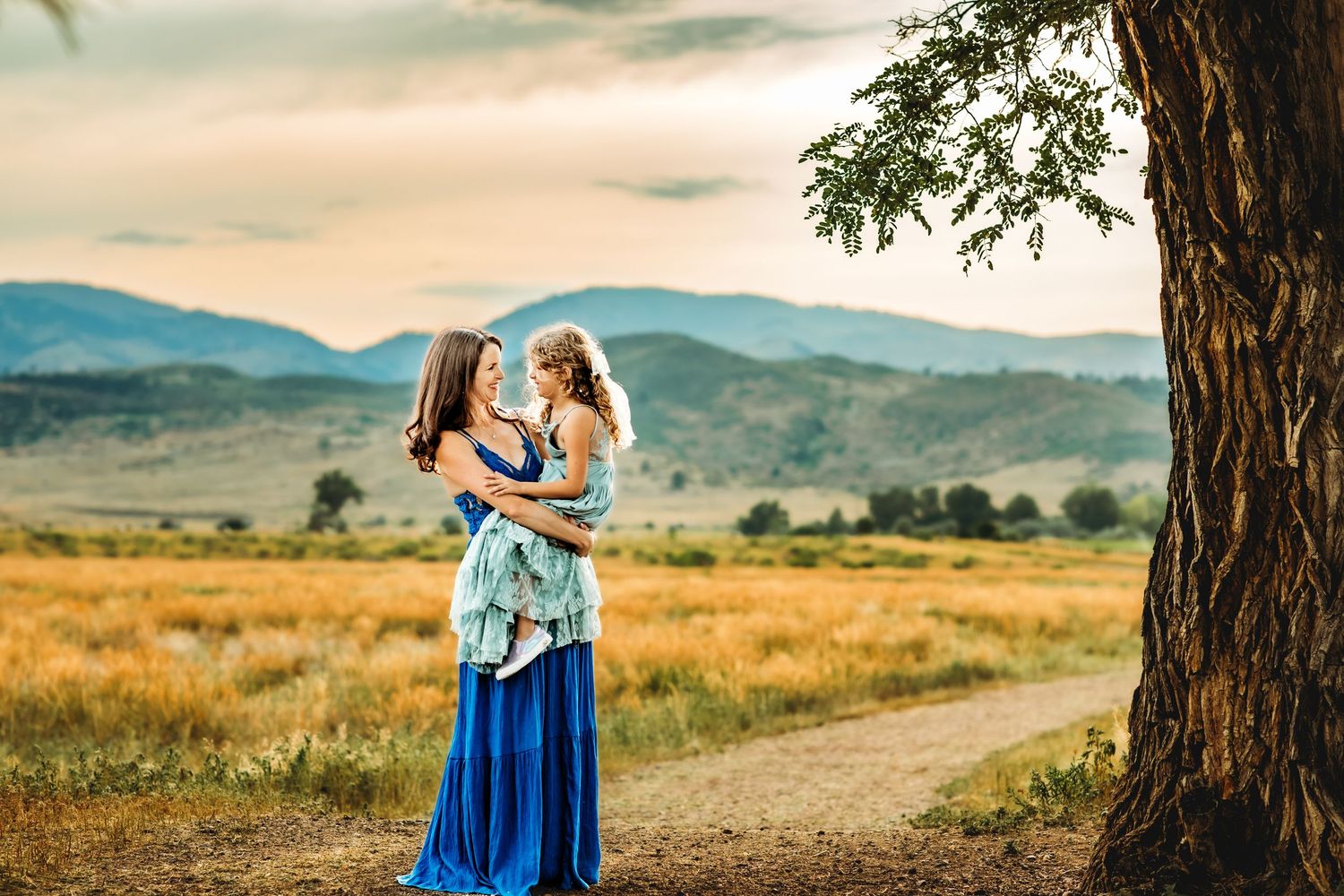A couple in blue attire shares an intimate moment against a scenic mountain landscape at sunset.