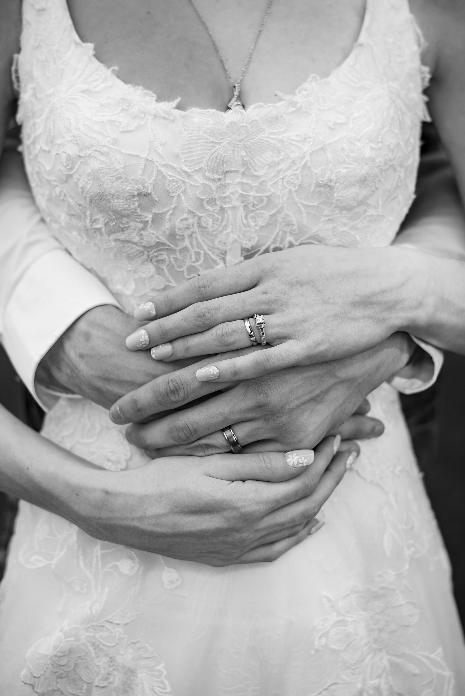 Black and white detail shots of hands with wedding rings and lace dress.