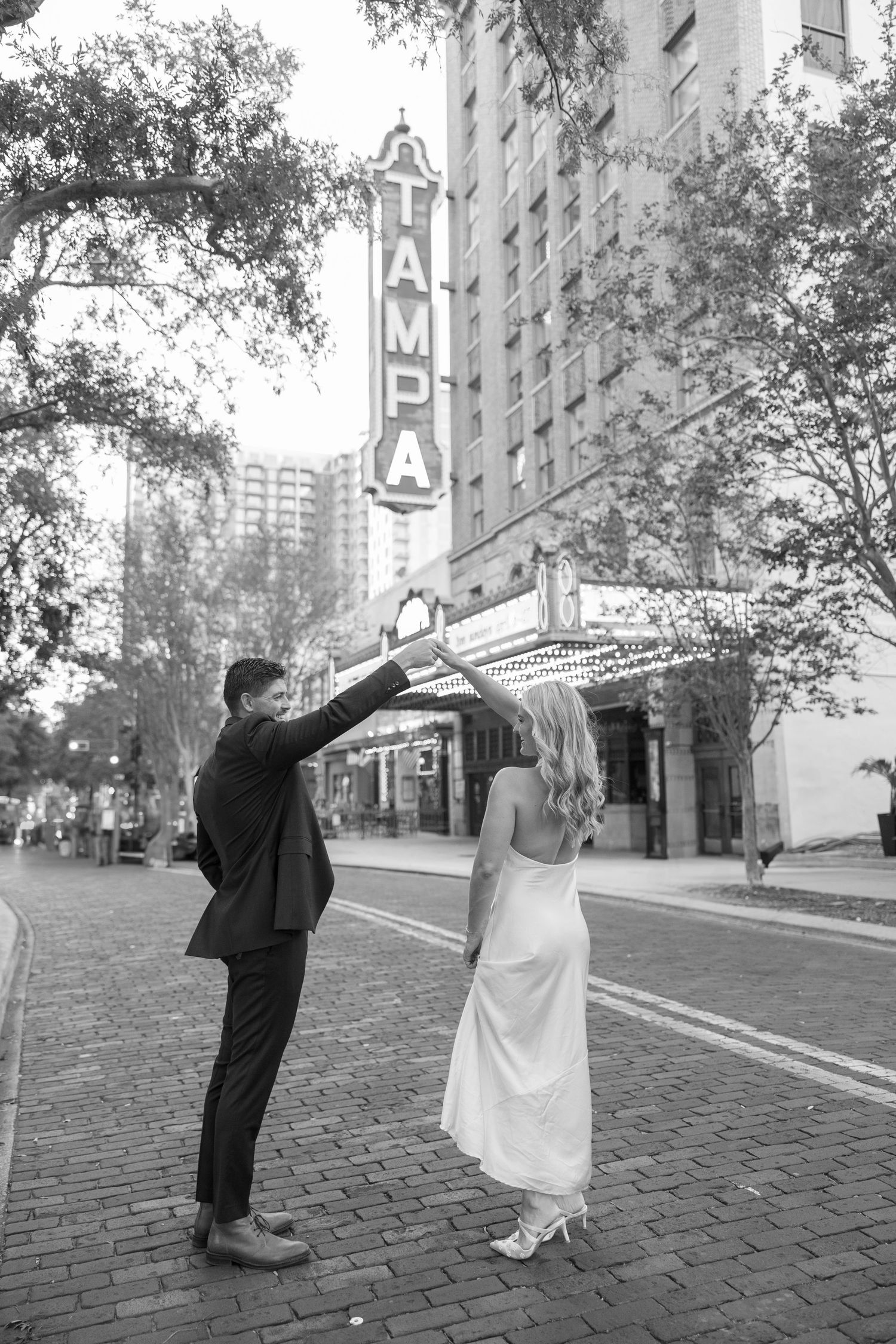 A sequence of black and white photos showing a couple dancing on a cobblestone street near urban buildings.