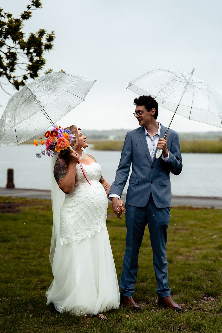 A couple poses with white umbrellas by a waterfront on their wedding day in a playful series of shots.