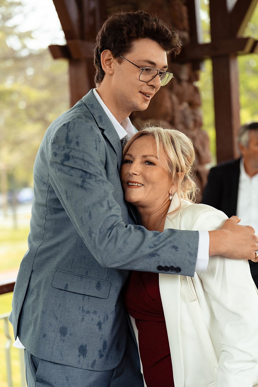 A couple shares a tender moment while dancing together under a wooden gazebo in an outdoor setting.