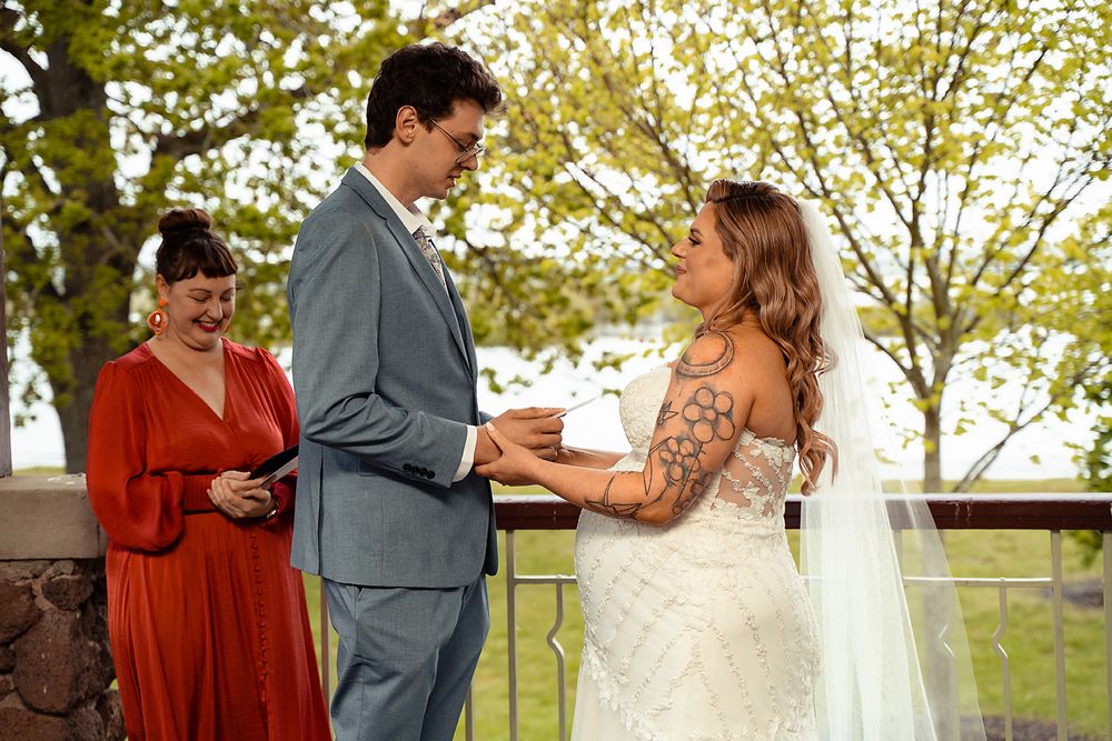 A couple in formal attire dances together in a park setting surrounded by autumn trees and natural light.