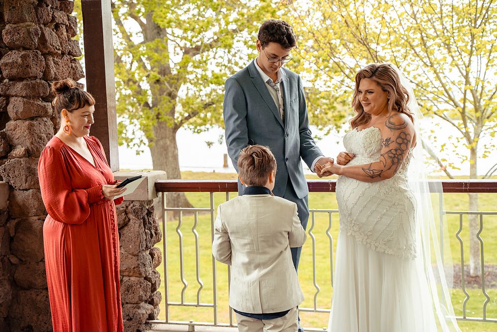 A wedding ceremony takes place on a rustic porch with autumn trees in the background.