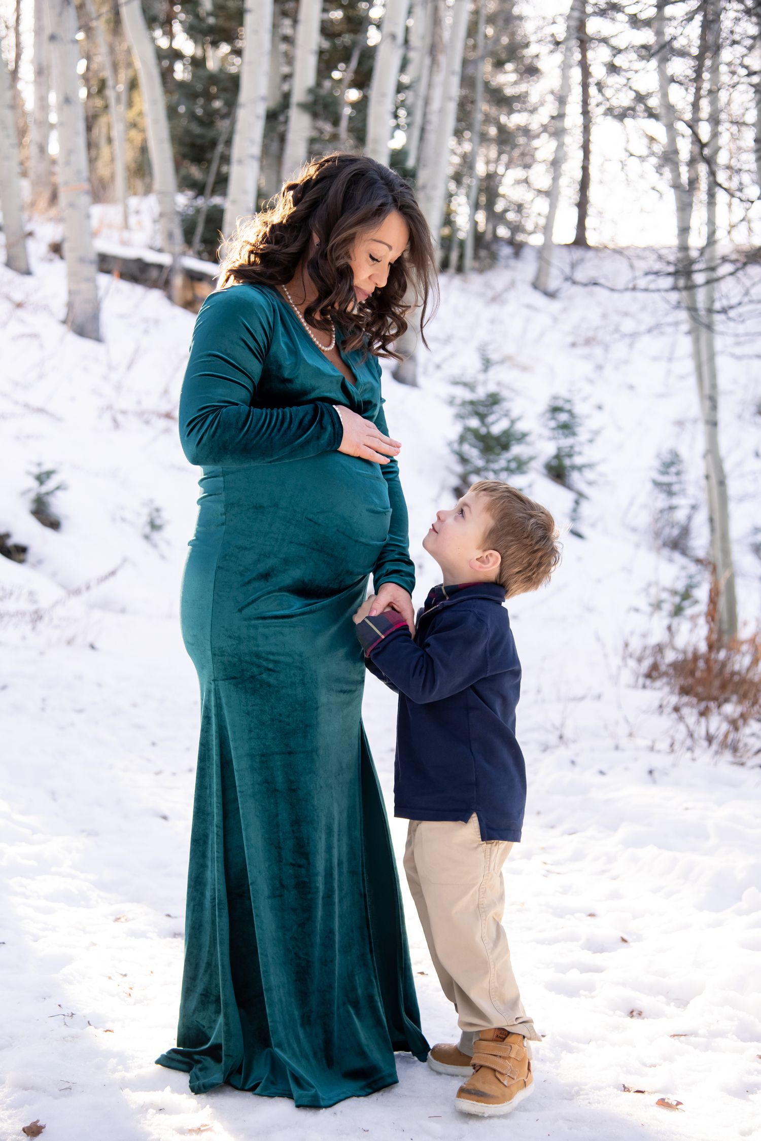 A parent and child share a tender moment in the snowy woods in Aspen Colorado maternity photo session