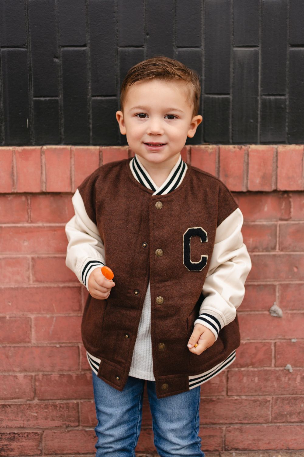 Collage of four photos showing a brown varsity jacket with striped cuffs worn with blue jeans against a brick wall.