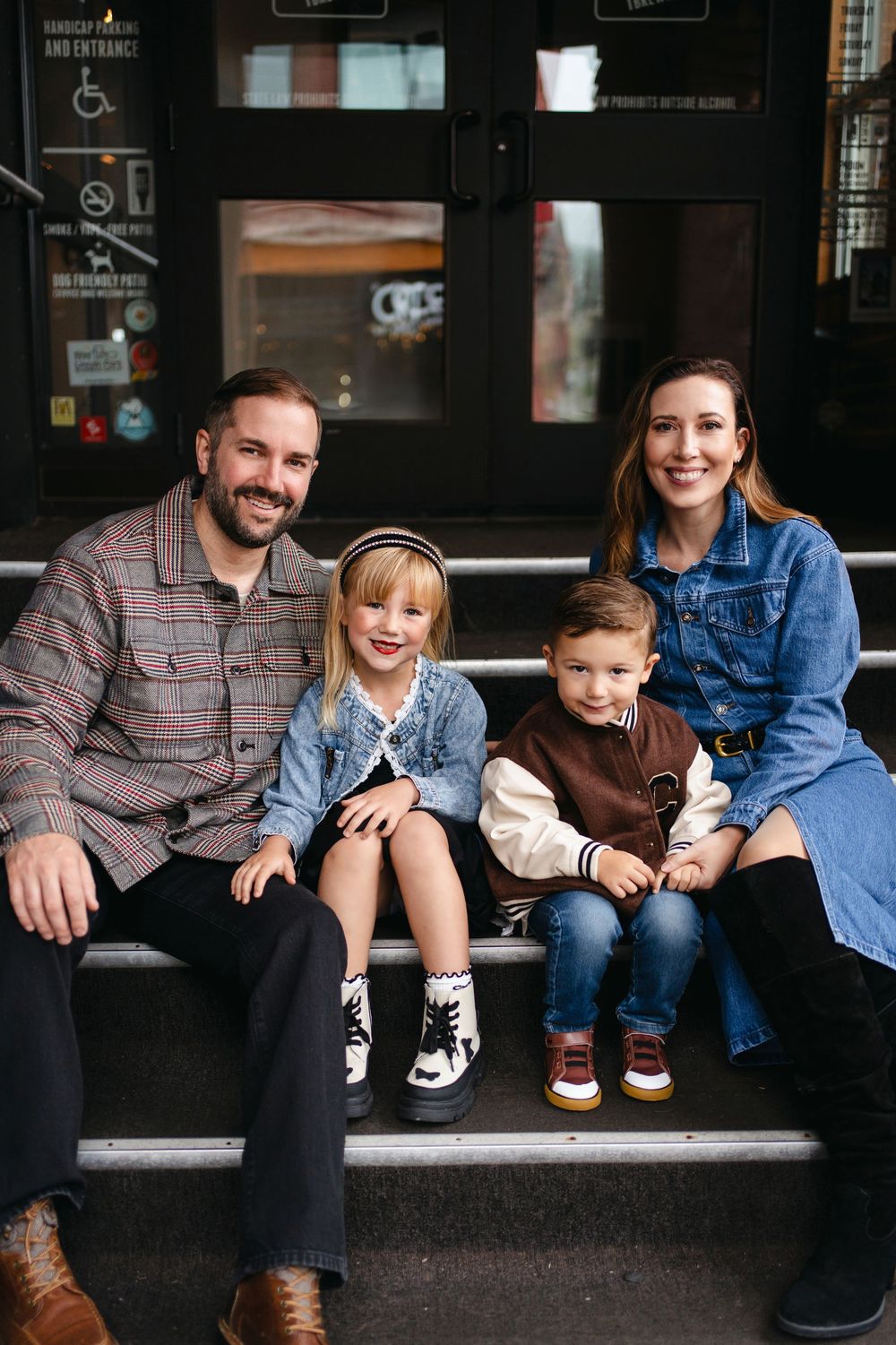 A family sits together on concrete steps outside a building, wearing casual clothing in complementary blue and plaid.