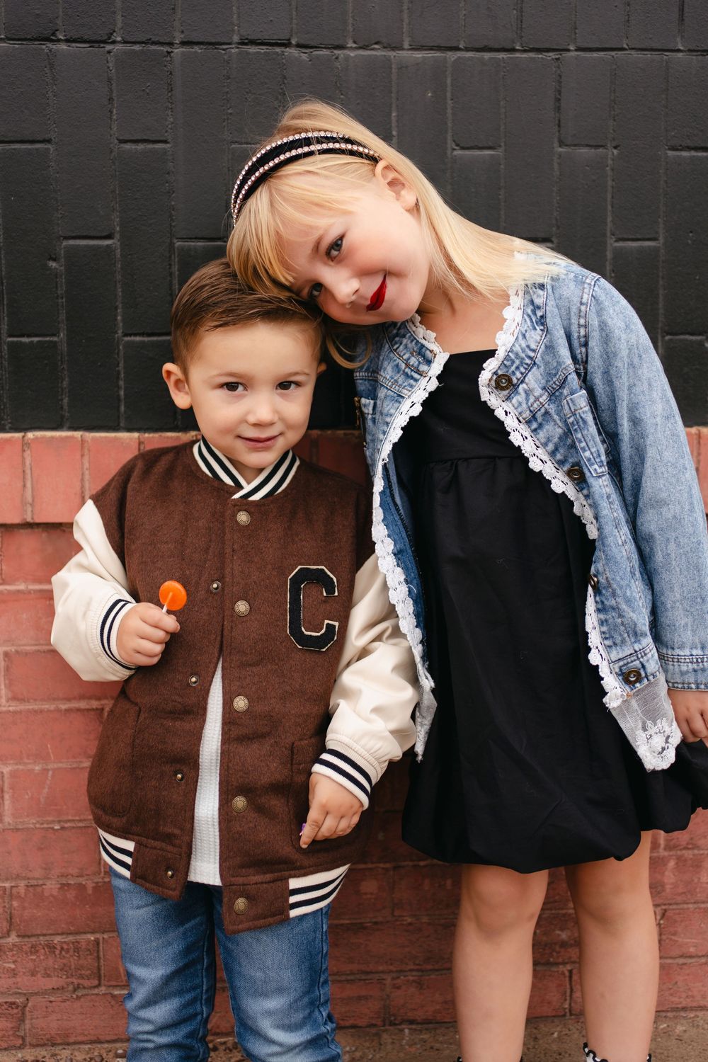 Two siblings share a sweet moment while posing against a brick wall in trendy casual wear.