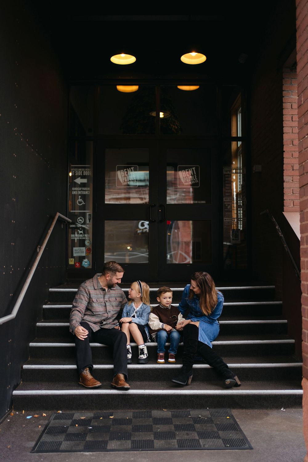 Family sits together on a dark storefront stoop, creating an intimate outdoor moment.