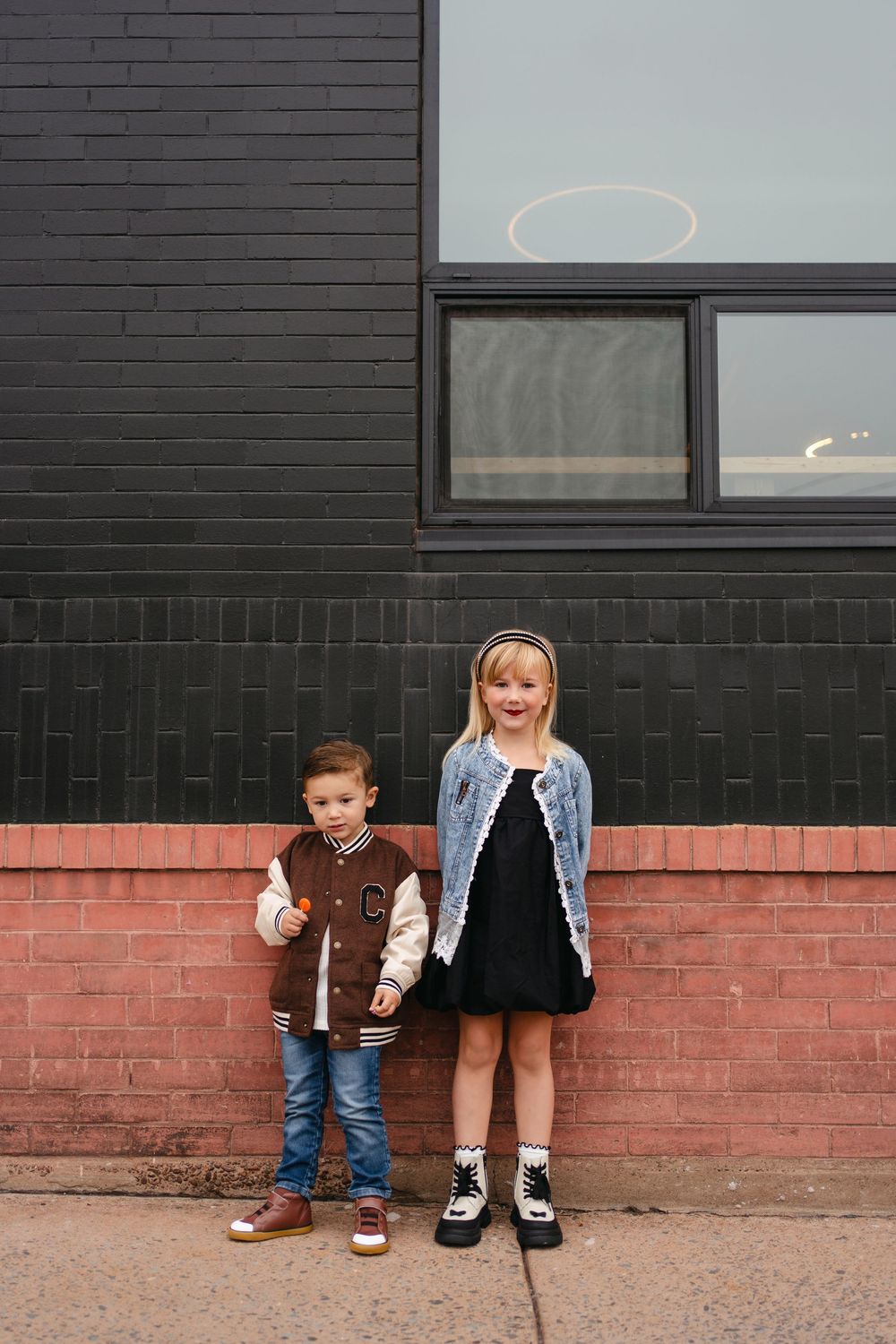 Two children pose against an industrial backdrop wearing coordinated casual outfits.
