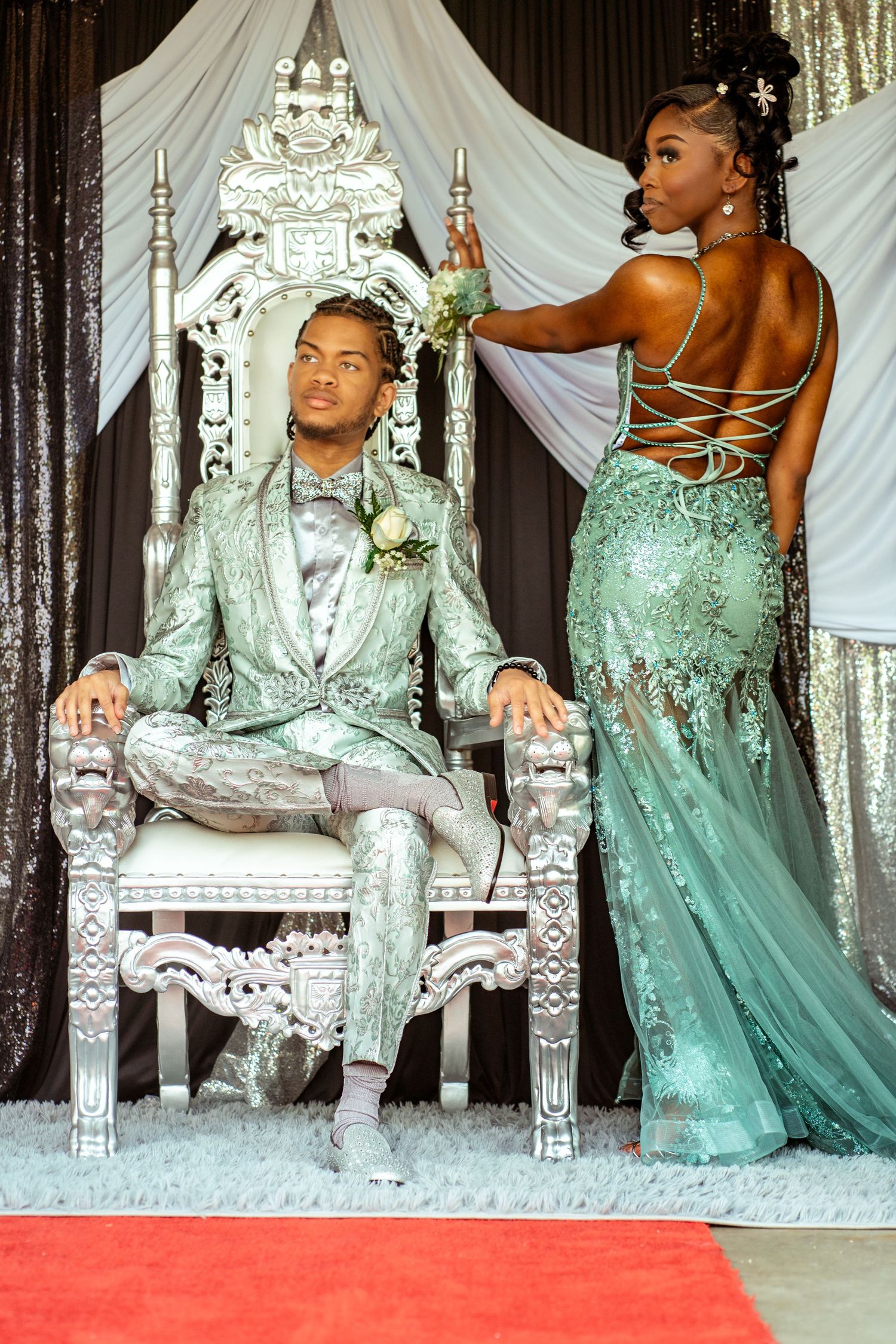 Glamorous prom photo with mint green gown and silver throne chair on red carpet.