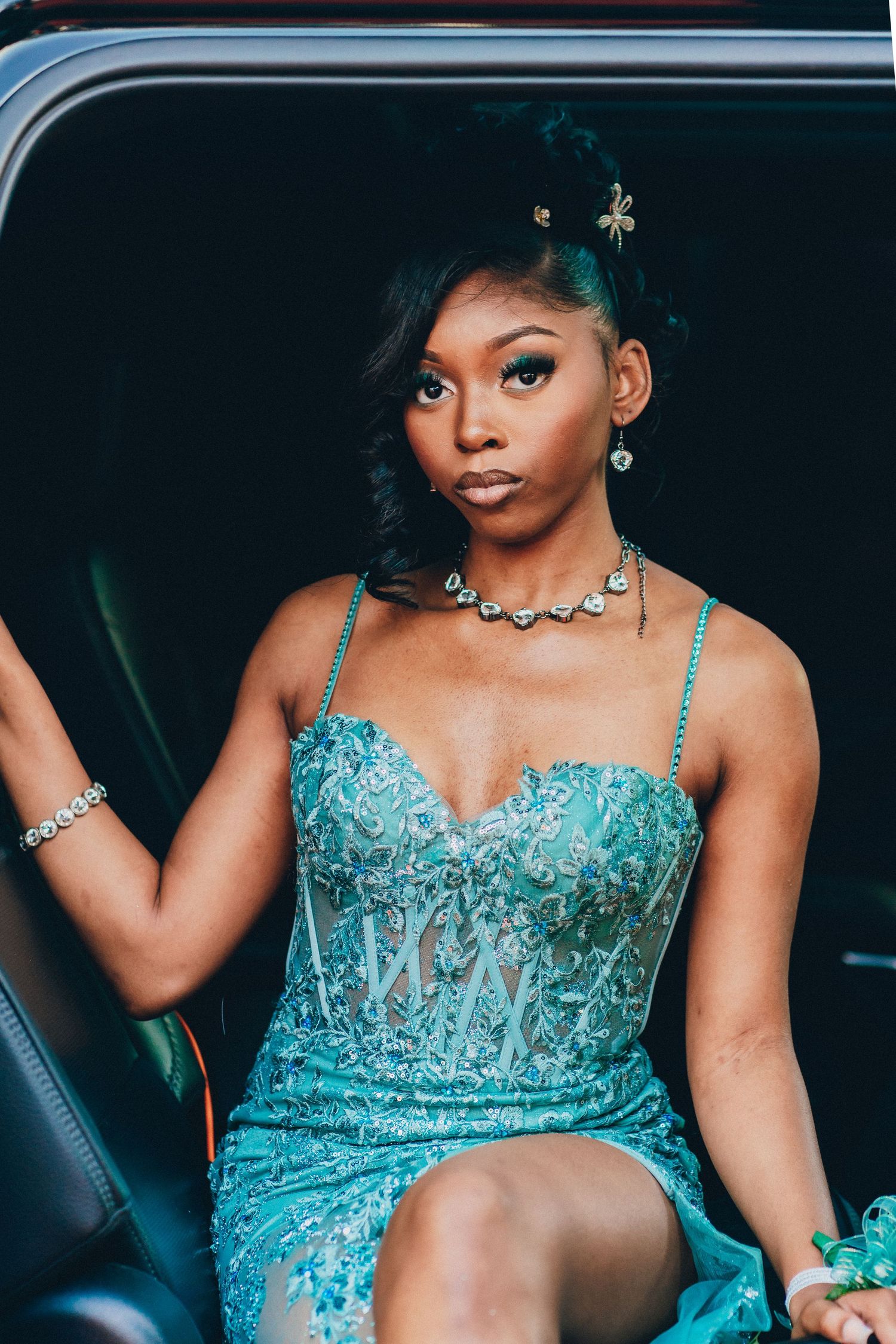 Elegant pose in turquoise beaded gown with jewelry inside luxury vehicle.
