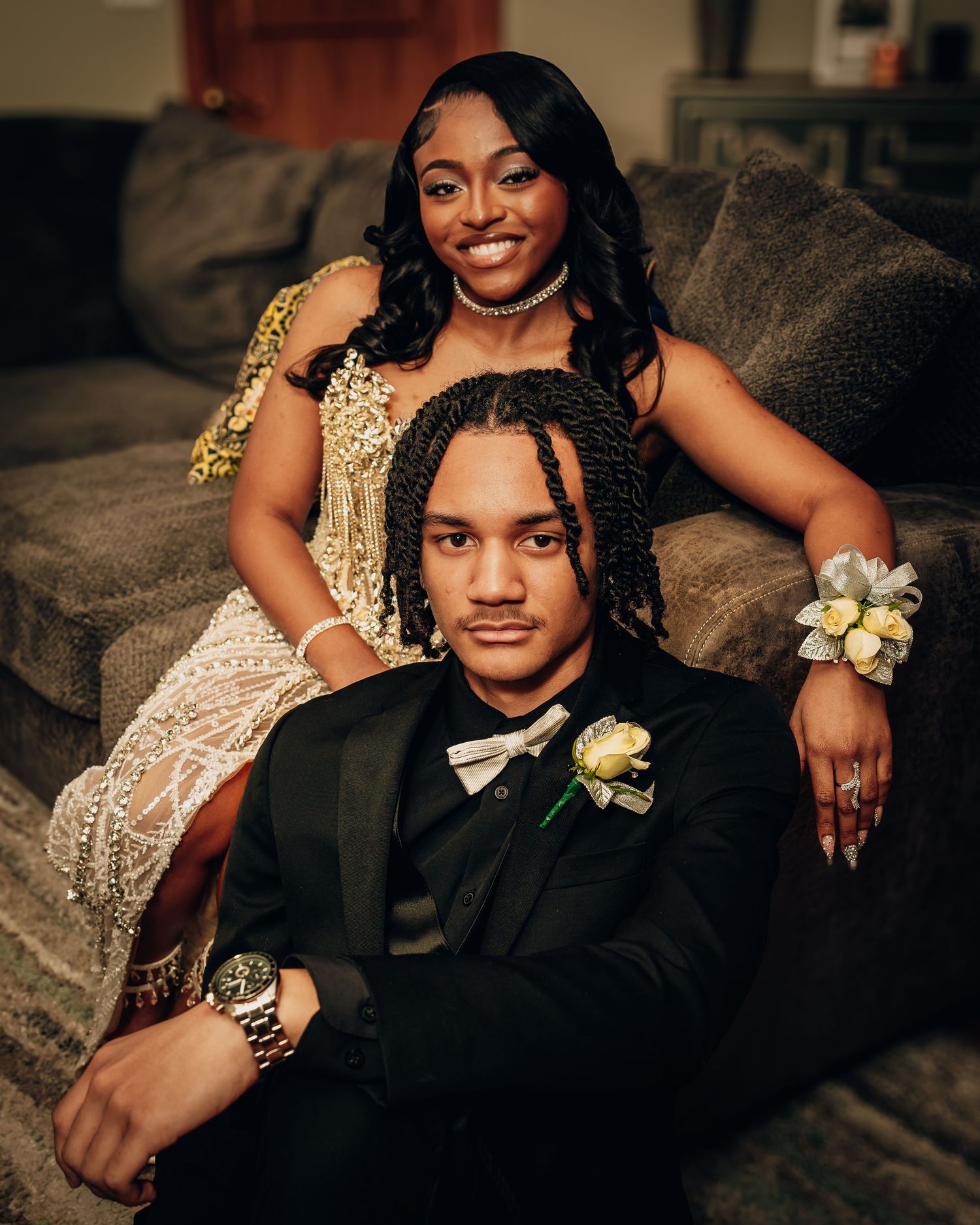 Formal portrait on couch showing sparkly gold dress and black tuxedo with boutonniere.