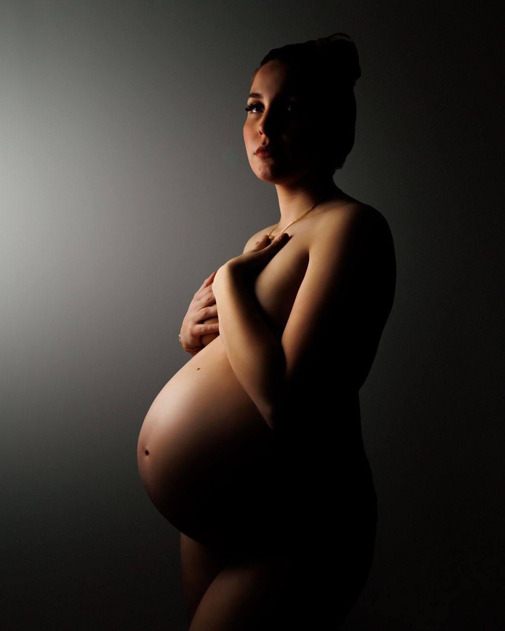 Artistic maternity silhouette photo with dramatic side lighting highlighting a pregnant figure against dark background.
