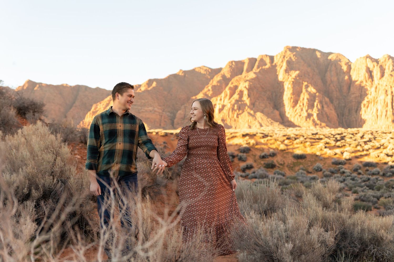Stunning engagement photos in kayenta ivins man and woman walking towards camera laughing at each other holding hands. red mountain