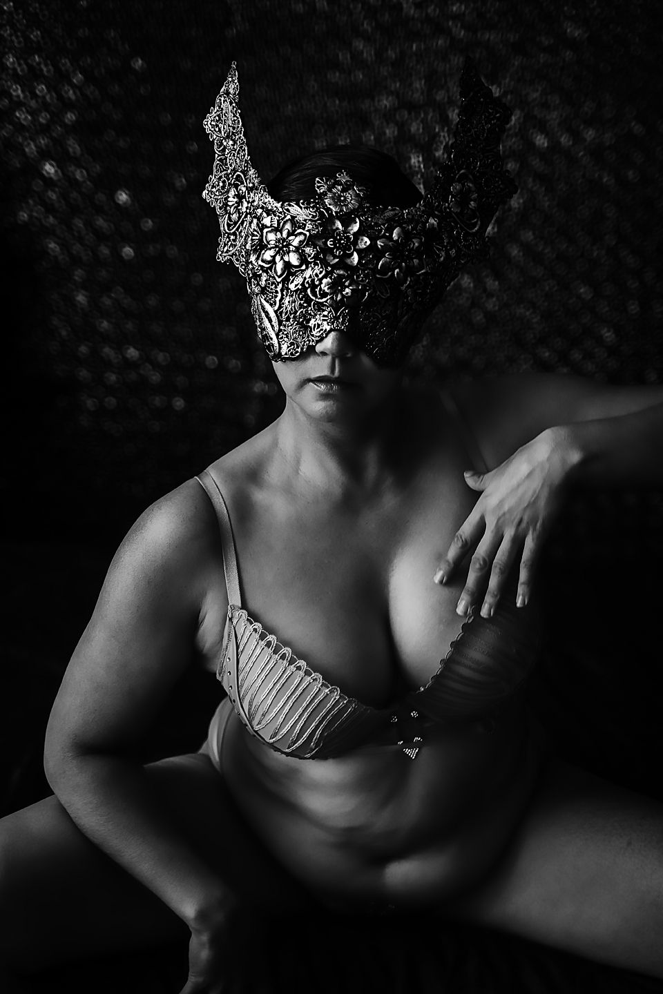 Artistic black and white portrait featuring an ornate lace mask and lingerie against a dark textured background.