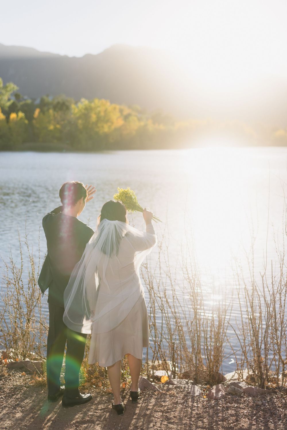 Silhouettes of couple sitting by a lake at sunset with tall grass and golden light streaming through the scene.
