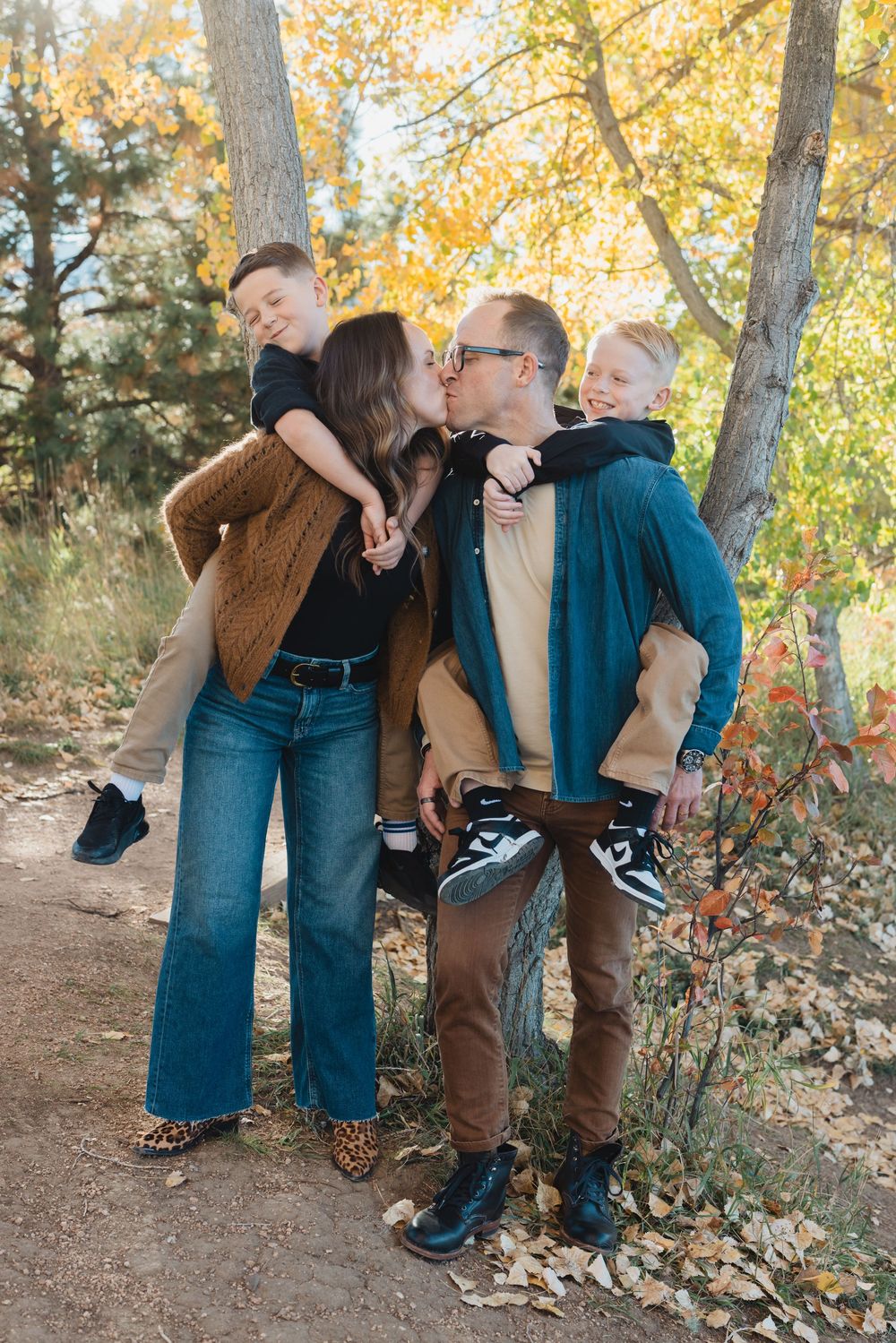A playful family photoshoot series in a fall forest setting with warm autumn colors and fallen leaves.