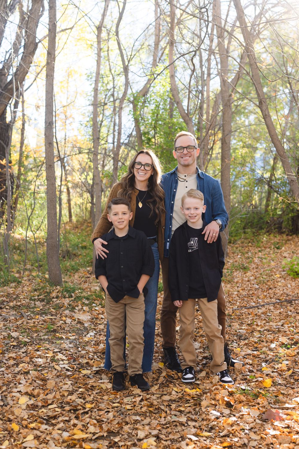 A group poses together in an autumn forest setting surrounded by fallen yellow leaves on the ground.