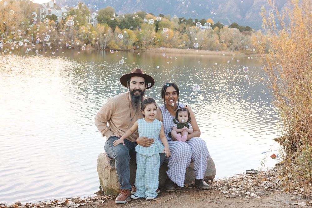 A group of people sitting together by a lake on an autumn day with fall foliage in the background.
