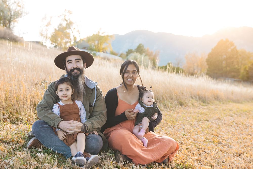 A family enjoys quality time together in a golden field during sunset as mountains rise in the background.