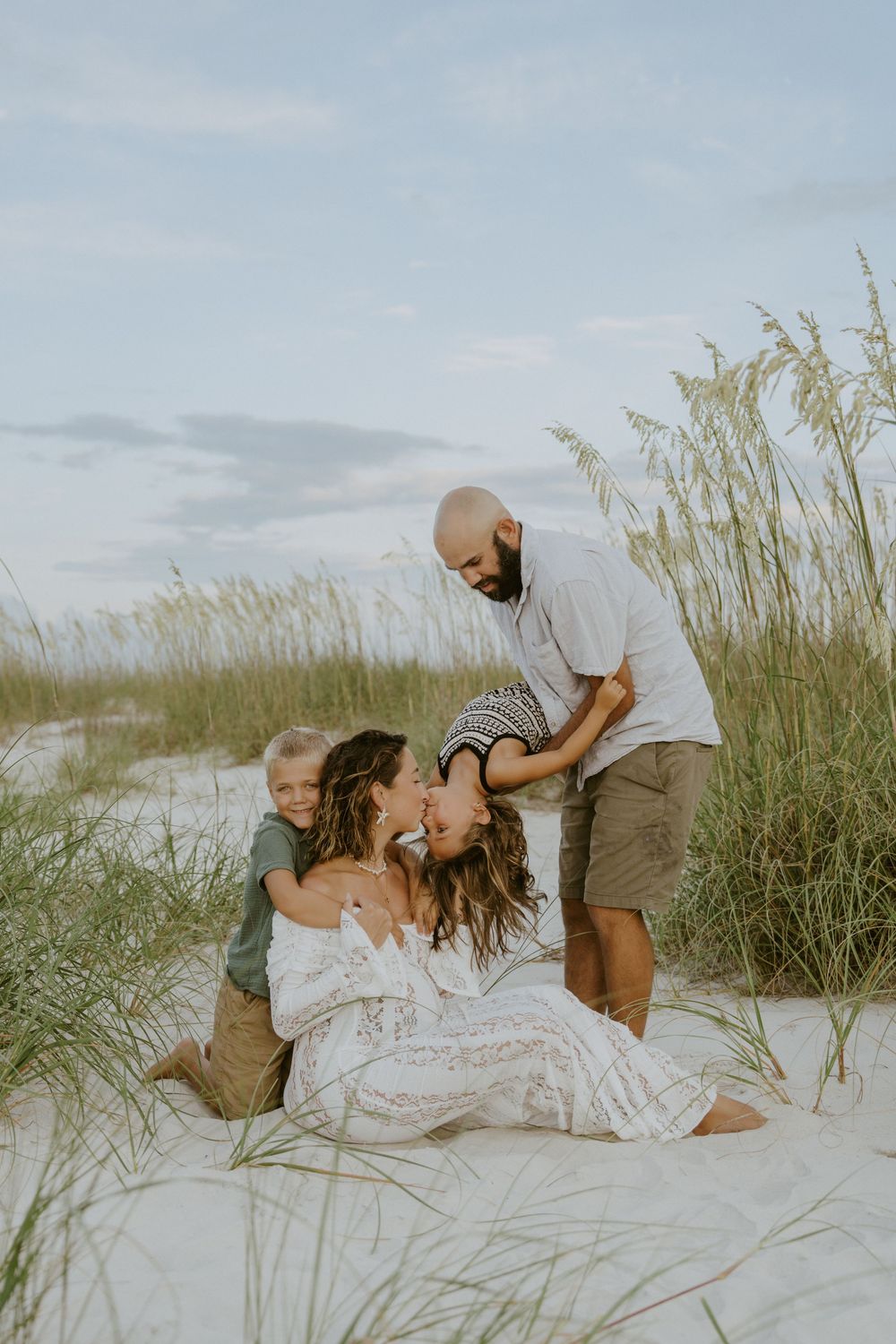 A tender family moment captured on white sand dunes with sea grass swaying in the background during sunset.