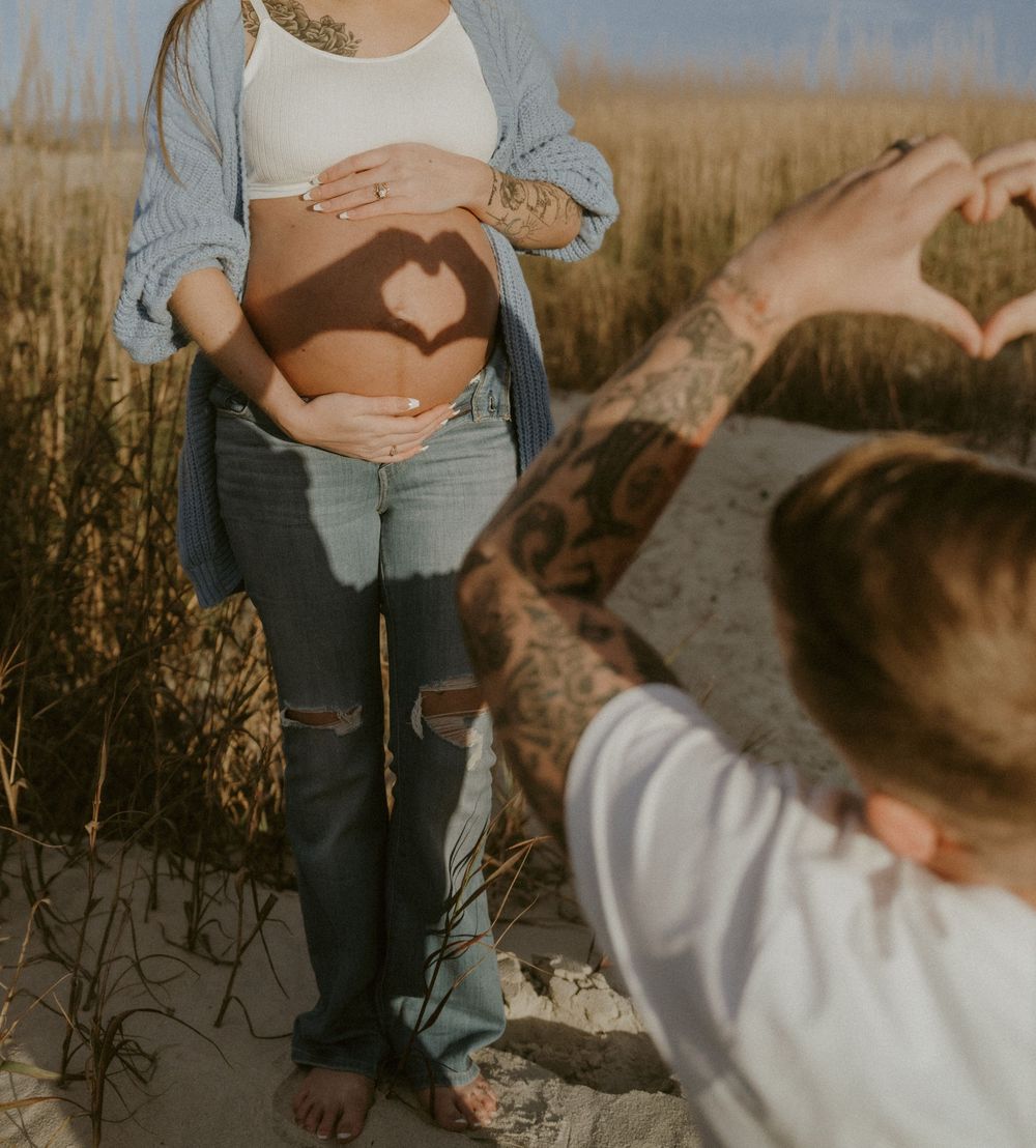 A person in jeans holds a small puppy while standing in a golden field during sunset.