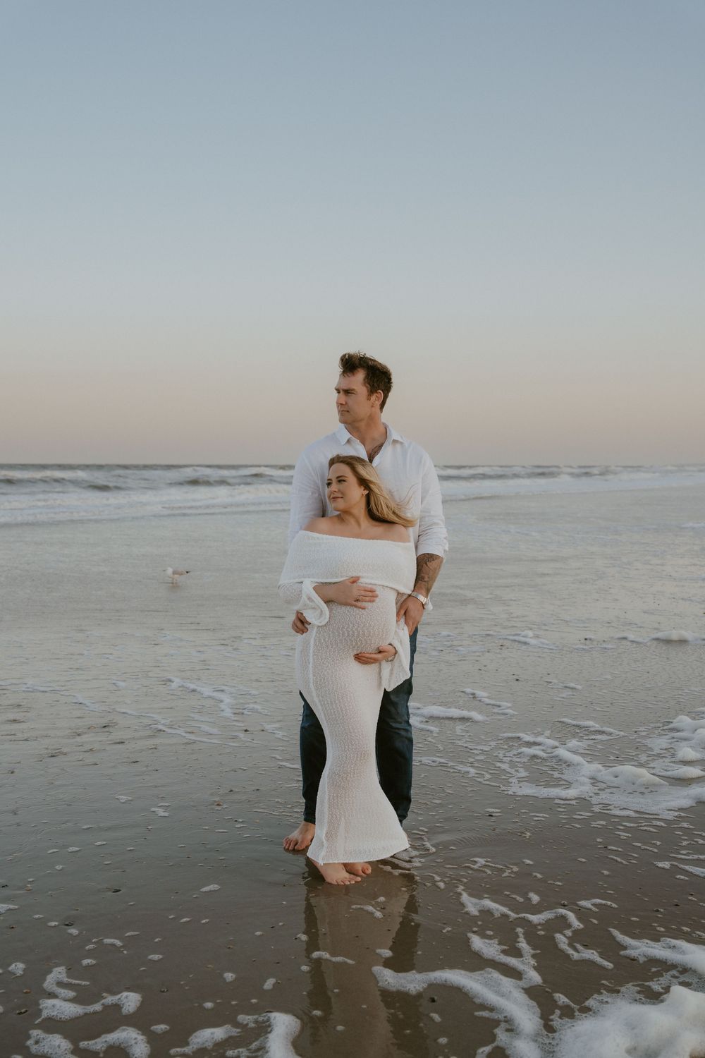 Couple plays and laughs together in shallow ocean waves at dusk.