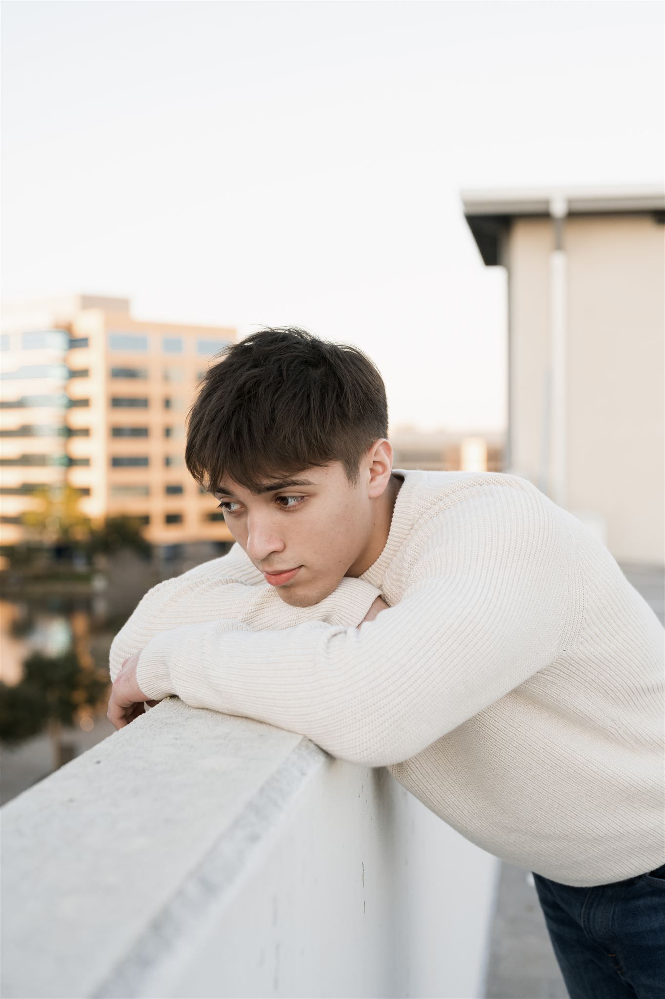 Person in white sweater leaning against concrete wall at sunset in urban setting.