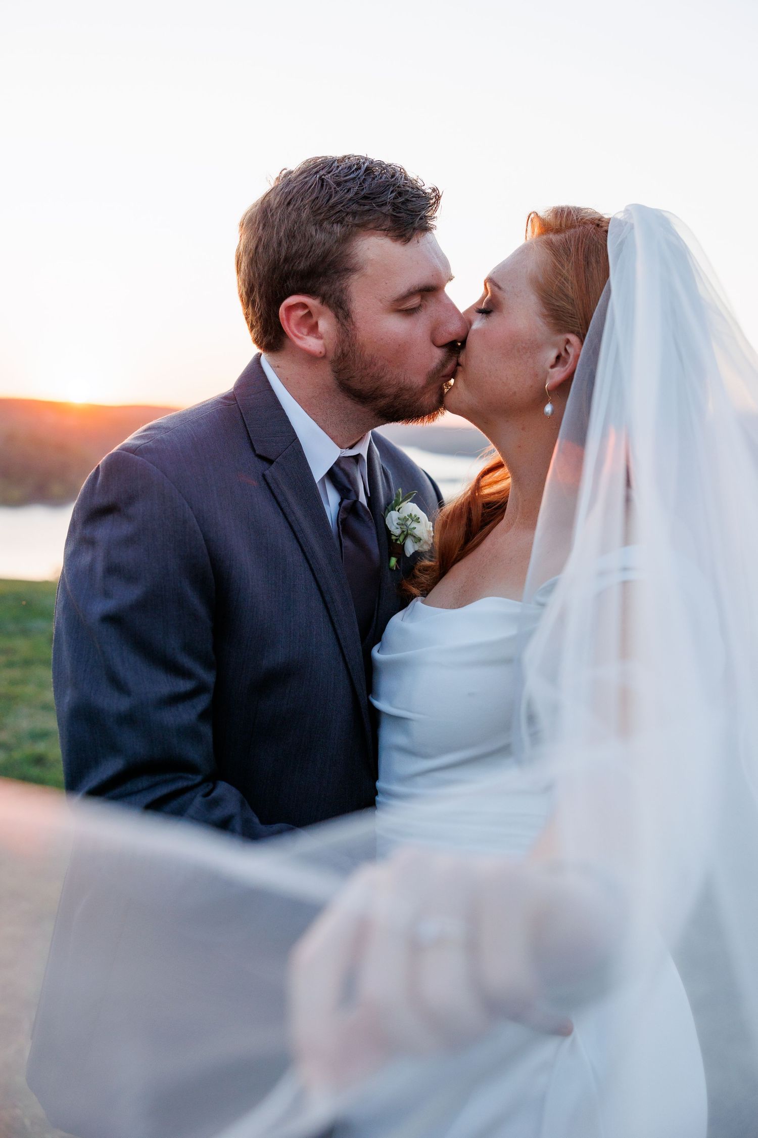 Romantic wedding couple shares a tender kiss at sunset while bride's veil flows in the breeze at Big Cedar Lodge.