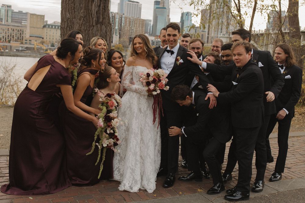 Elegant bridal party lined up against large tree trunks with urban backdrop.