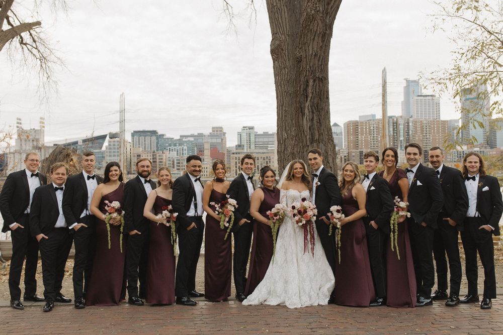Large wedding party arranged in line formation outdoors with downtown buildings visible.
