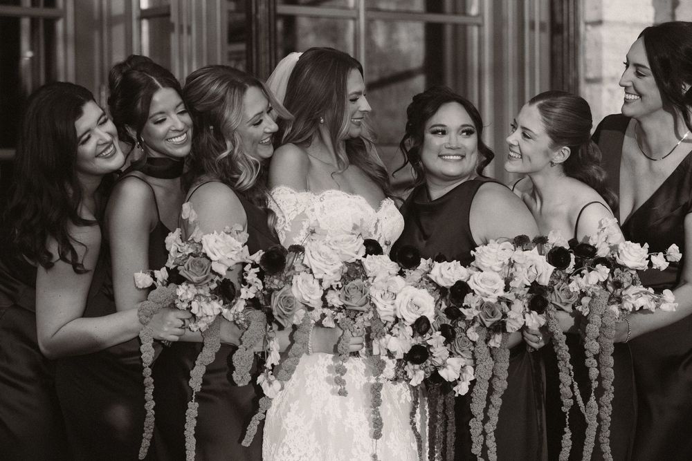 Wedding party poses with floral bouquets in coordinated brown dresses and white gowns.