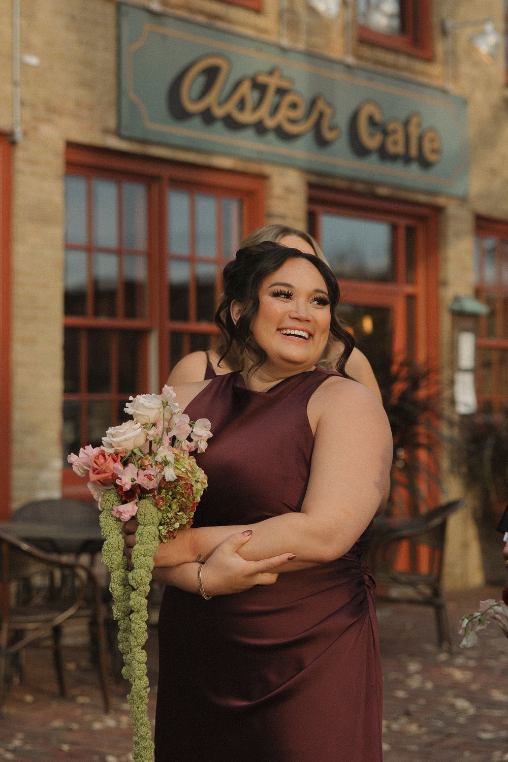 A person in a burgundy dress laughs joyfully while holding a bouquet with pink flowers and cascading greenery.