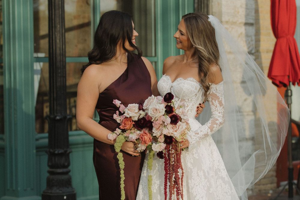 Bridesmaids in burgundy dresses and bride in white gown pose together holding burgundy and pink bouquets.