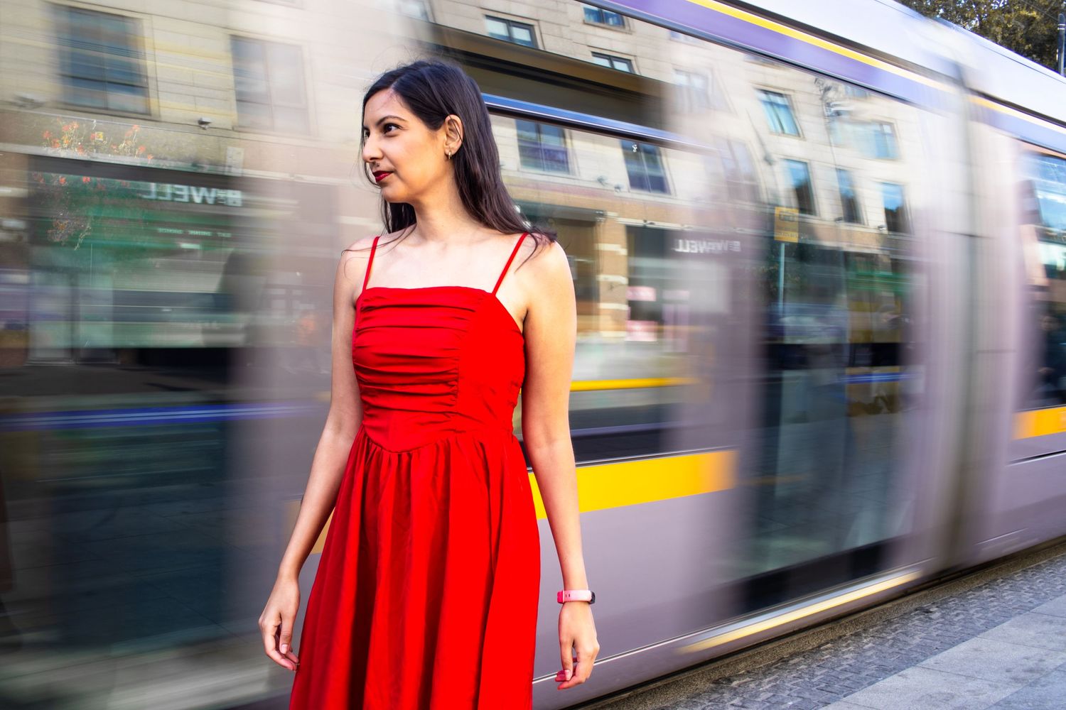 A woman in a red dress stands next to a passing train in motion.