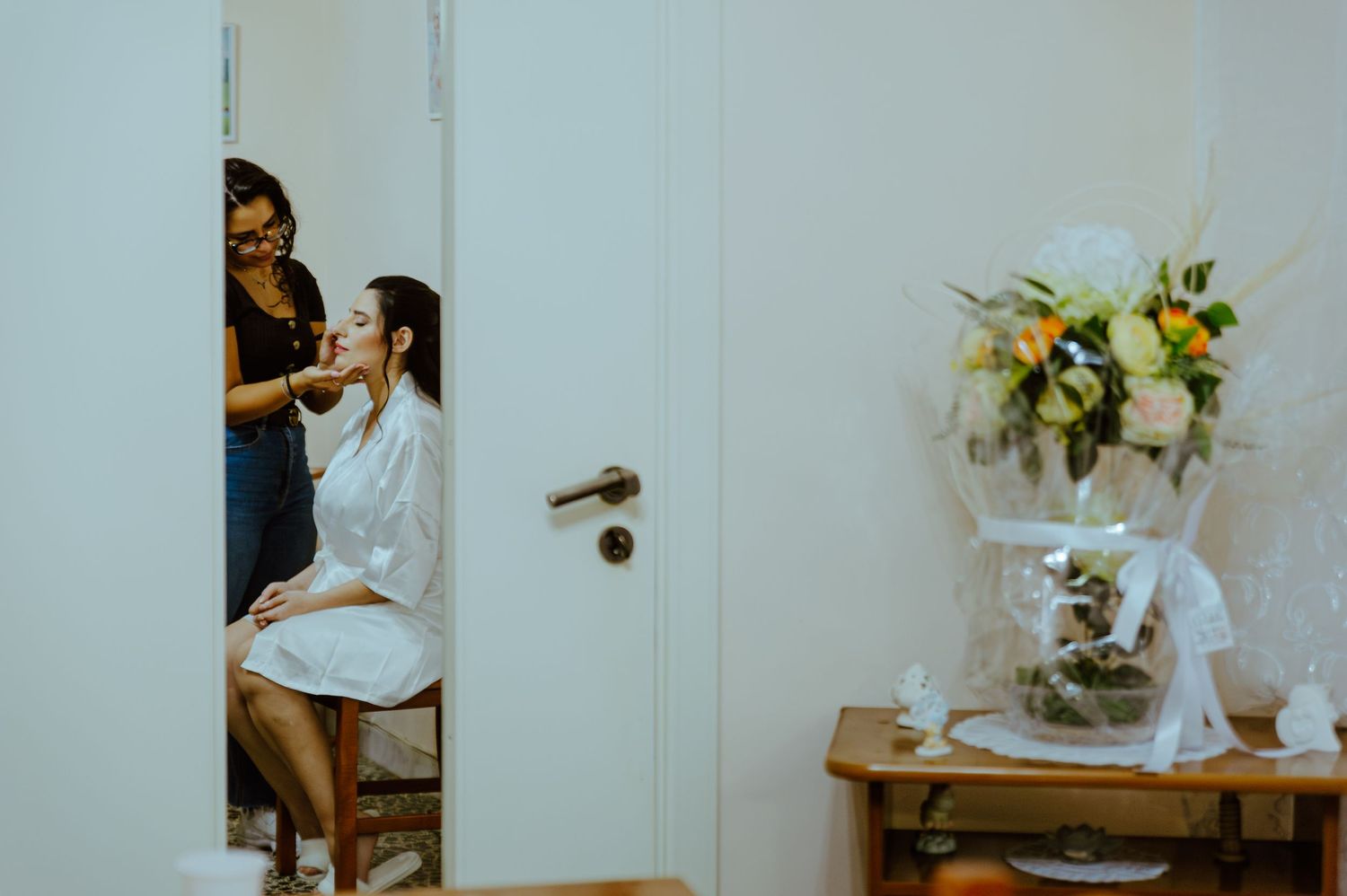 Through doorway glimpse of wedding preparation with floral arrangement on side table.